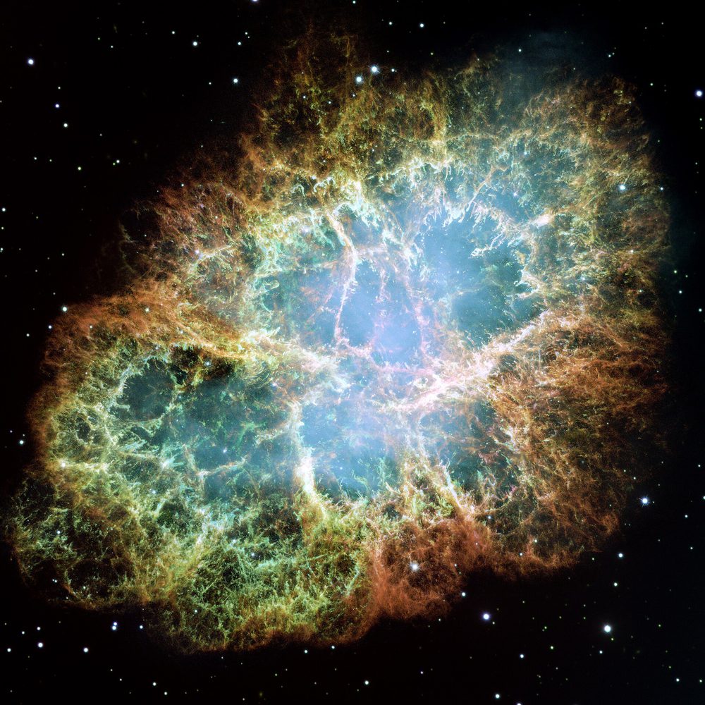 A glowing tangled cloud of filaments in orange, blue and green, the expanding remains of a star that exploded and was recorded on Earth in 1054.