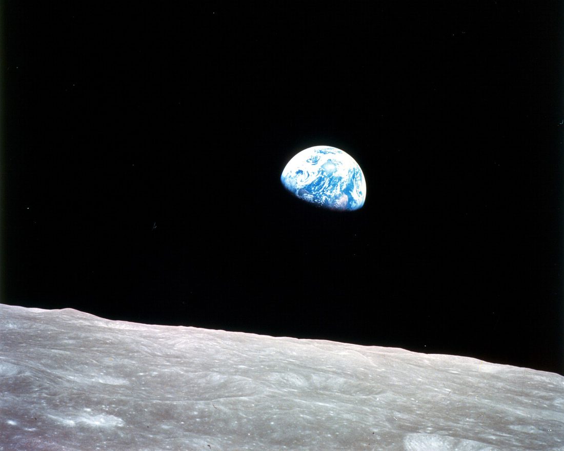 Earth seen as a blue and white sphere above the grey cratered surface of the Moon, photographed from lunar orbit.