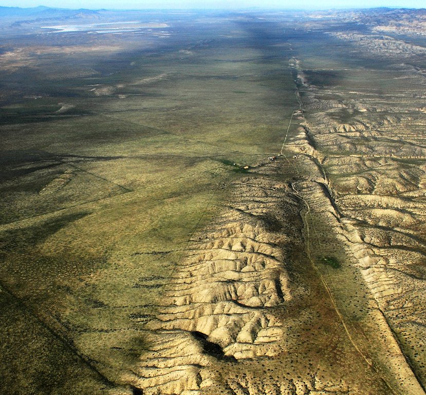 An aerial photograph of a long straight scar running across dry plains, where two plates slide past each other and a streambed is offset across the line.